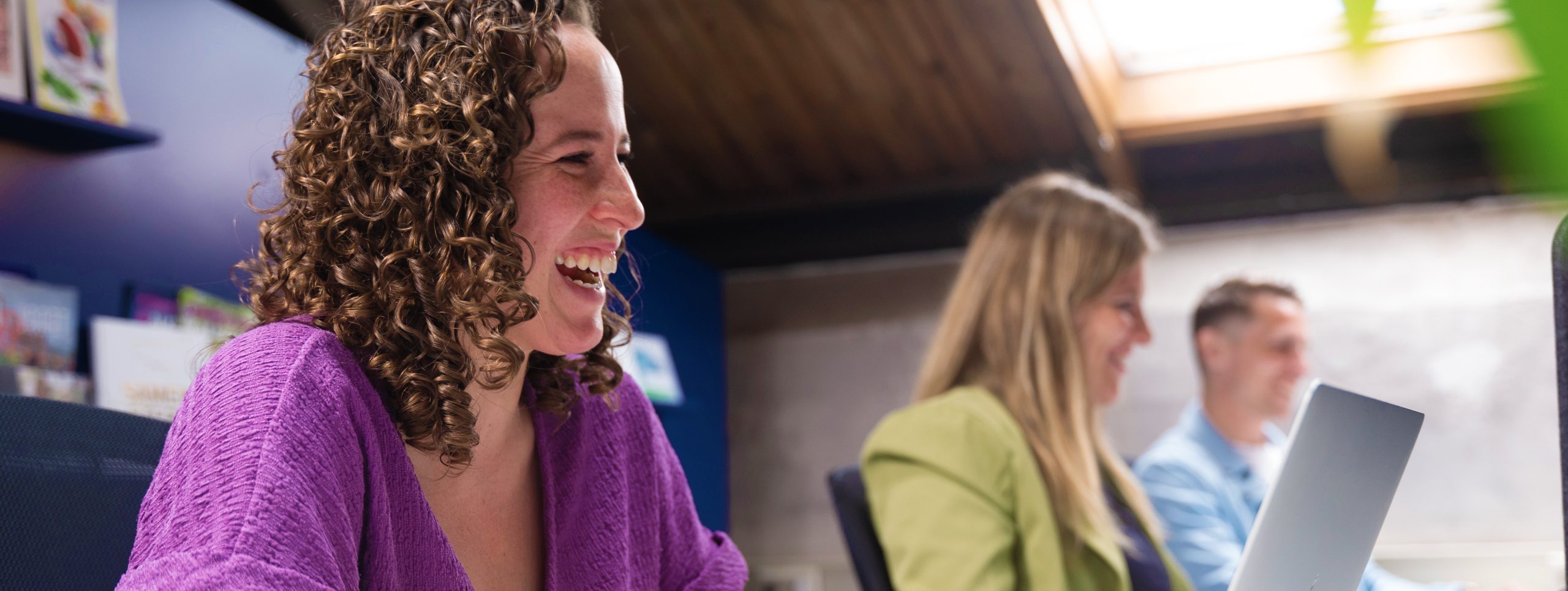 Medewerker Sasha van MEO lacht samen met collega's terwijl ze werken aan projecten.